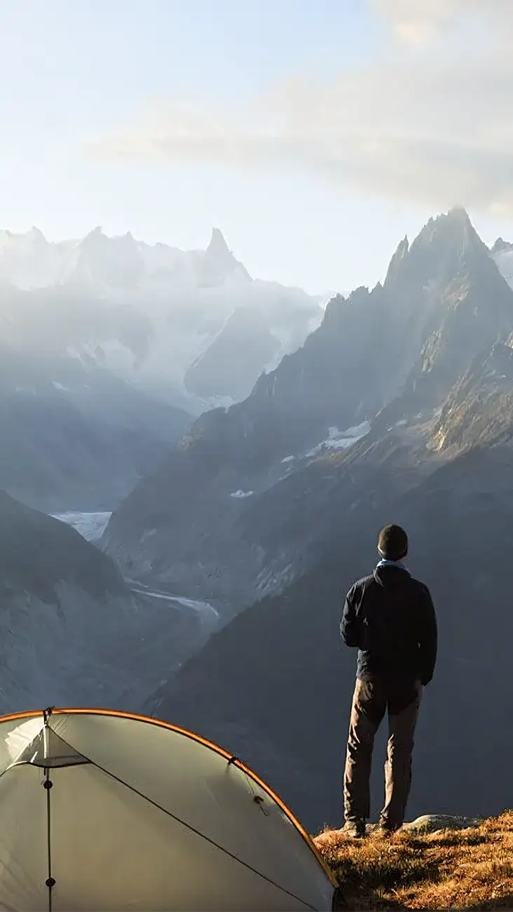 A white and orange tent pitched on a rocky mountain ledge.