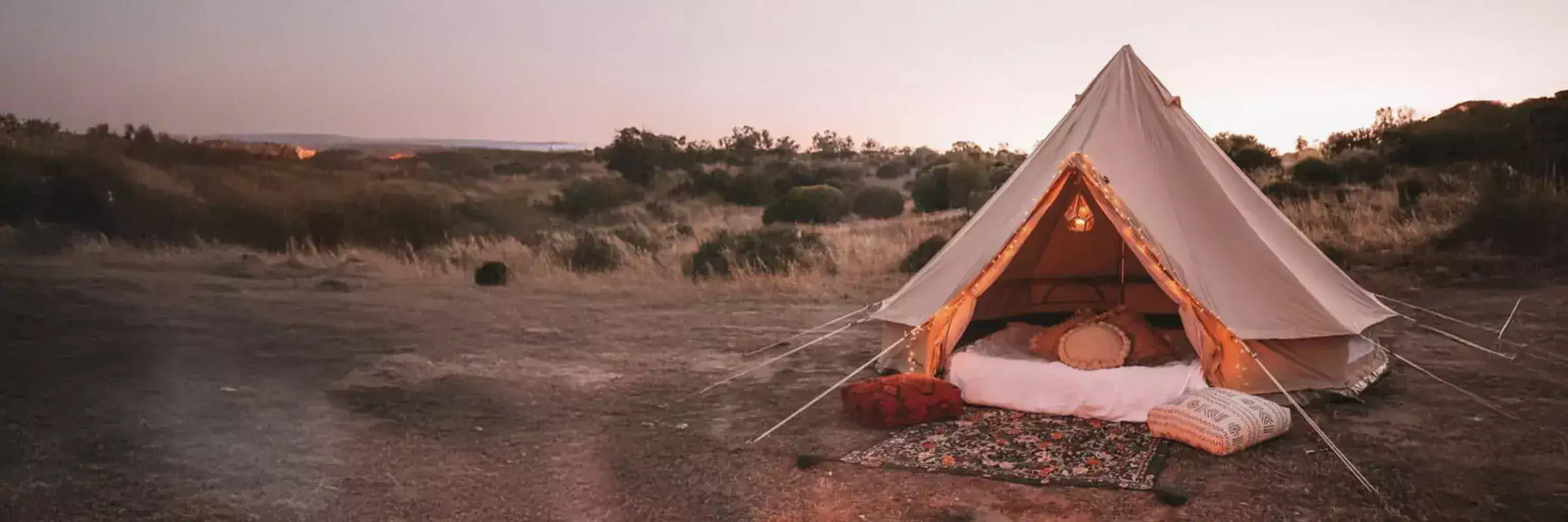 A beige bell tent with a triangular peak, set up in an open field at dusk.