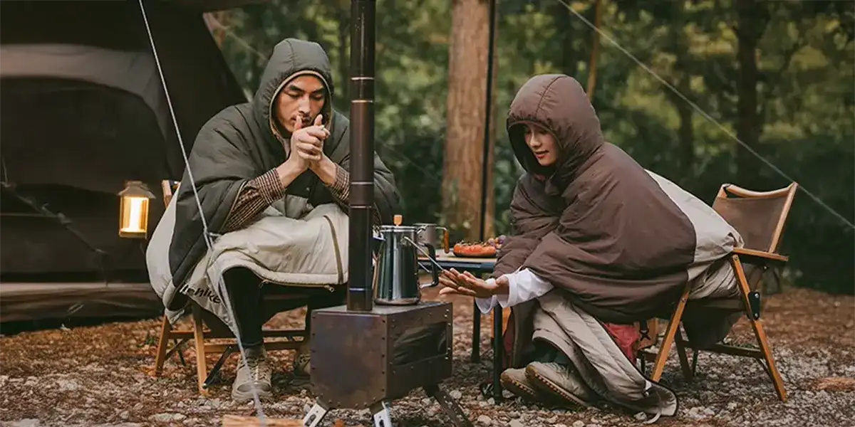 Black metal camping stove with a tall chimney and four legs